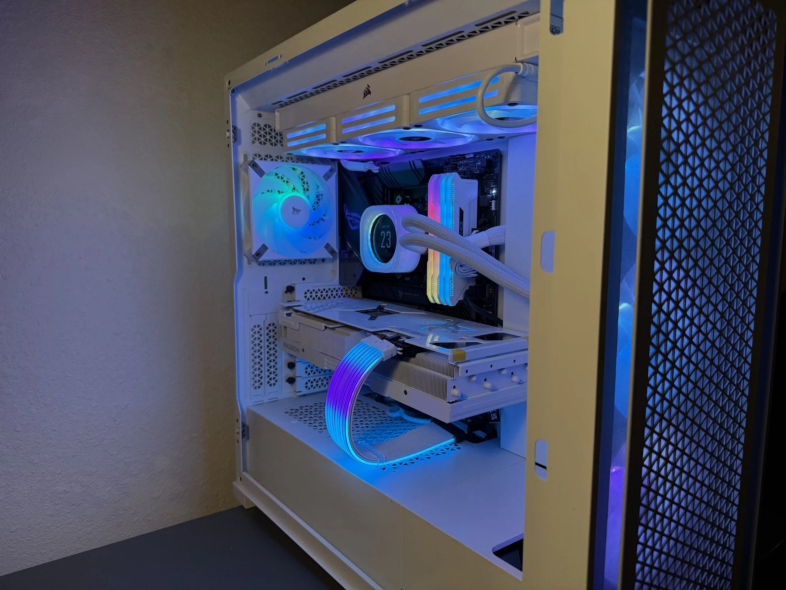A custom-built gaming computer with a white case, illuminated by blue and RGB lighting, featuring a cooling fan, an LCD monitor on the CPU cooler, and RGB RAM sticks inside.