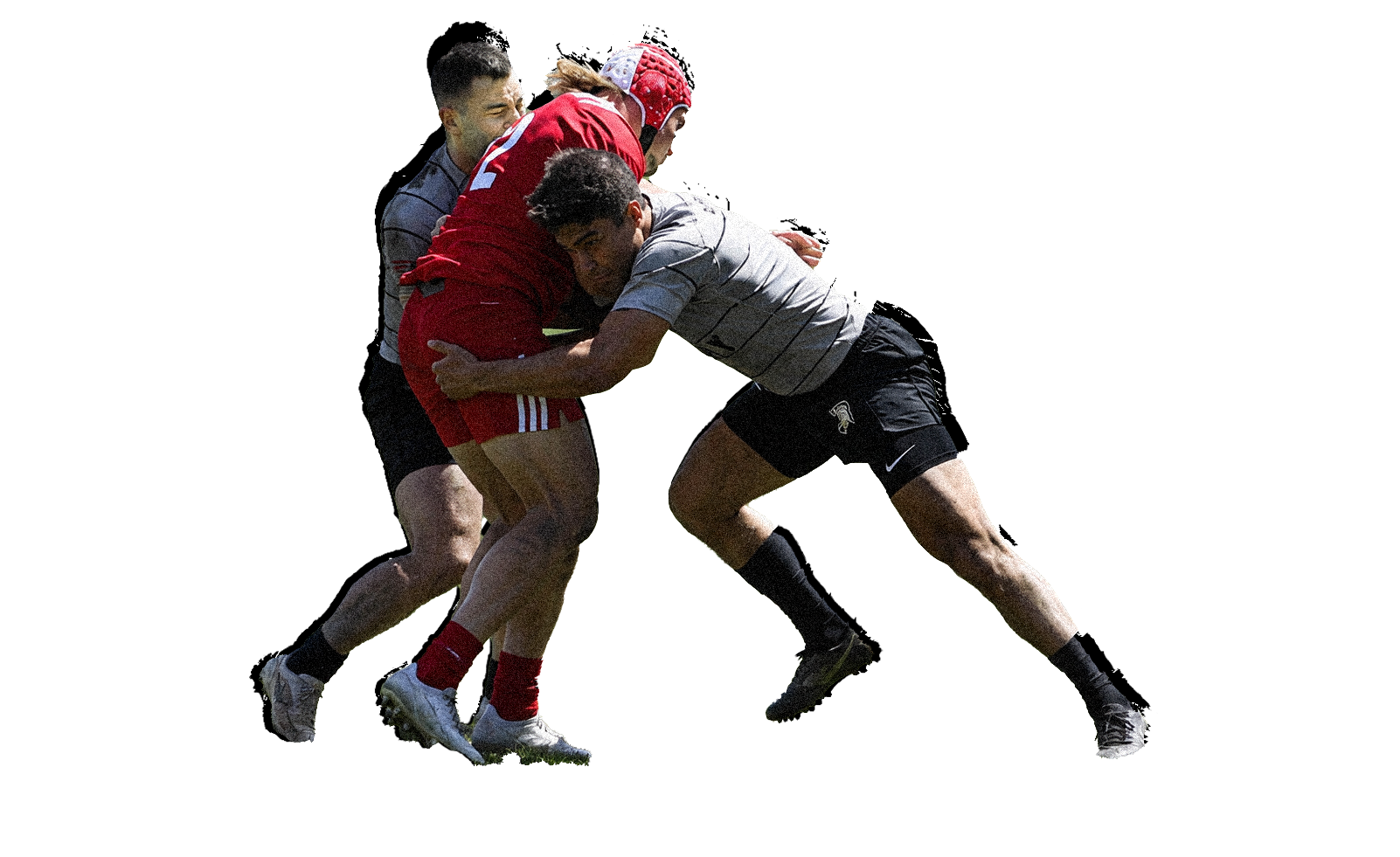 Three rugby players in action during a match, one in a red uniform, two in gray and black uniforms, engaged in a tackle on the field.