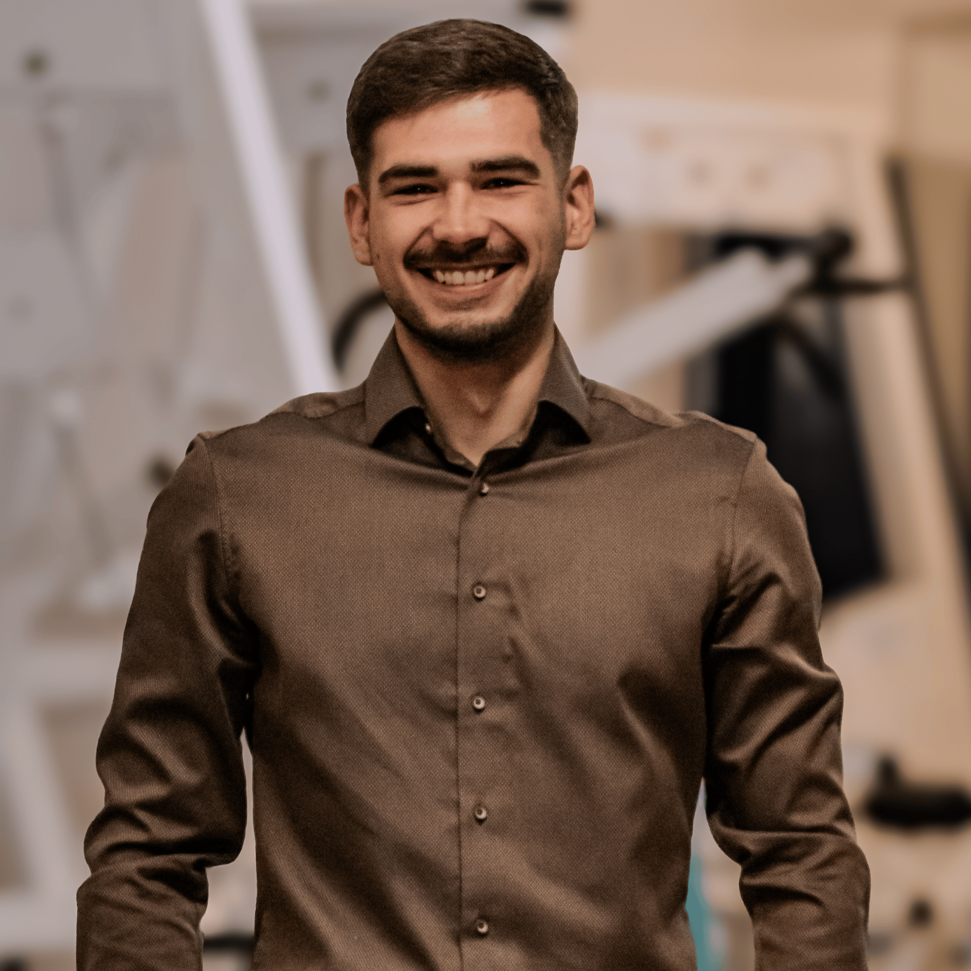 Ein lachender Mann mit braunem Hemd in einem Raum mit technischen Geräten im Hintergrund. Geschäftsführer Leitung Studioleiter Florian Weiß Weiss Flo Geschäftsleitung