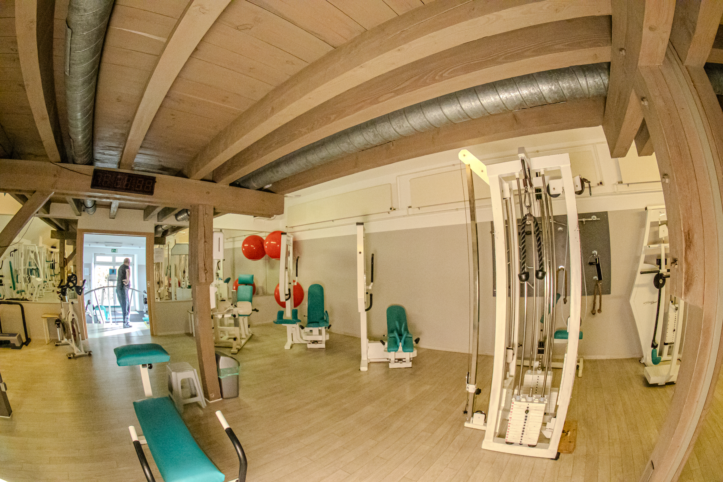 Innenraum eines Fitnessstudios mit verschiedenen Trainingsgeräten, rotem Exerciser-Ball, grünen Sitzbänken.