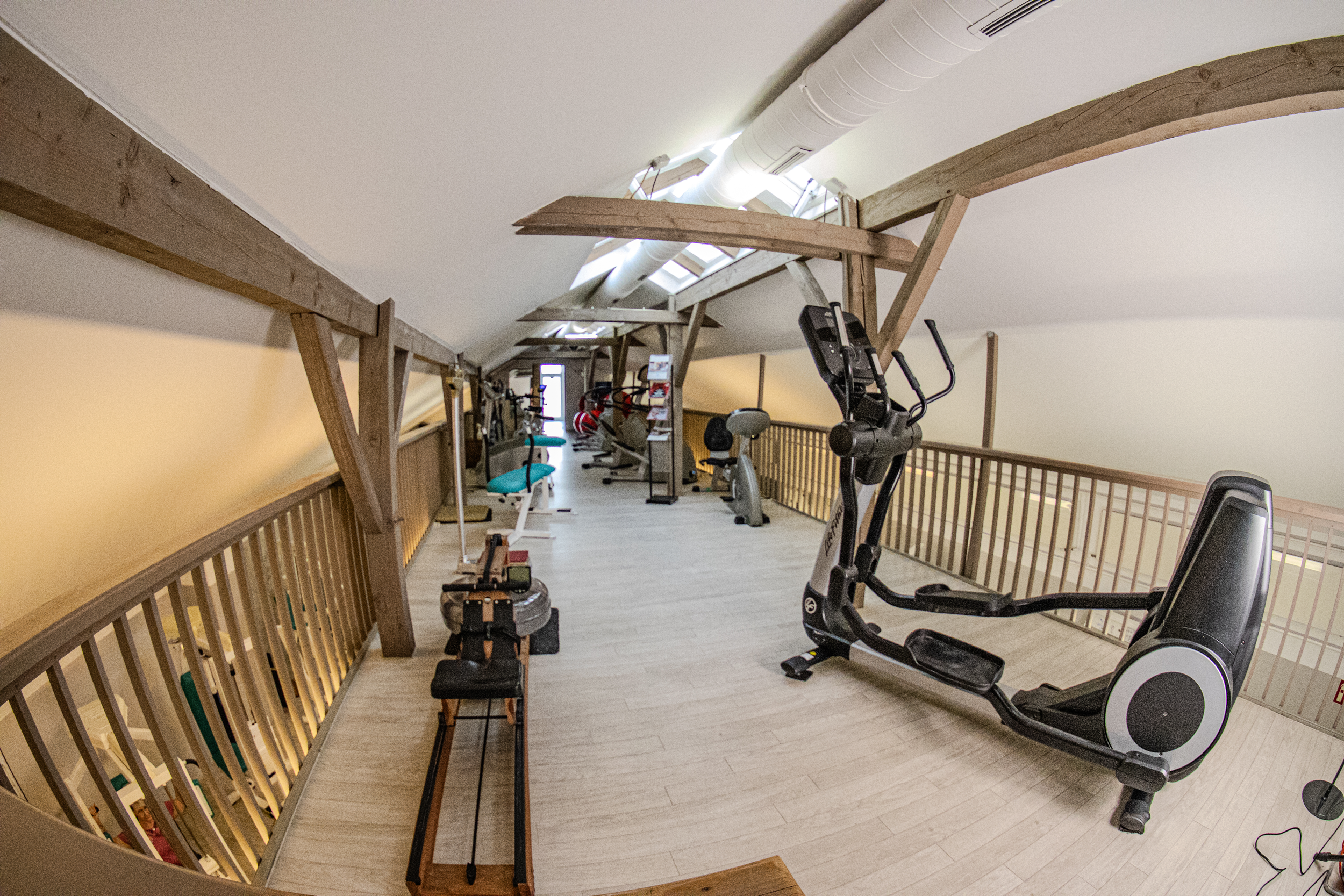Fitnessraum im Dachgeschoss mit verschiedenen Trainingsgeräten und Holzbalken an der Decke.