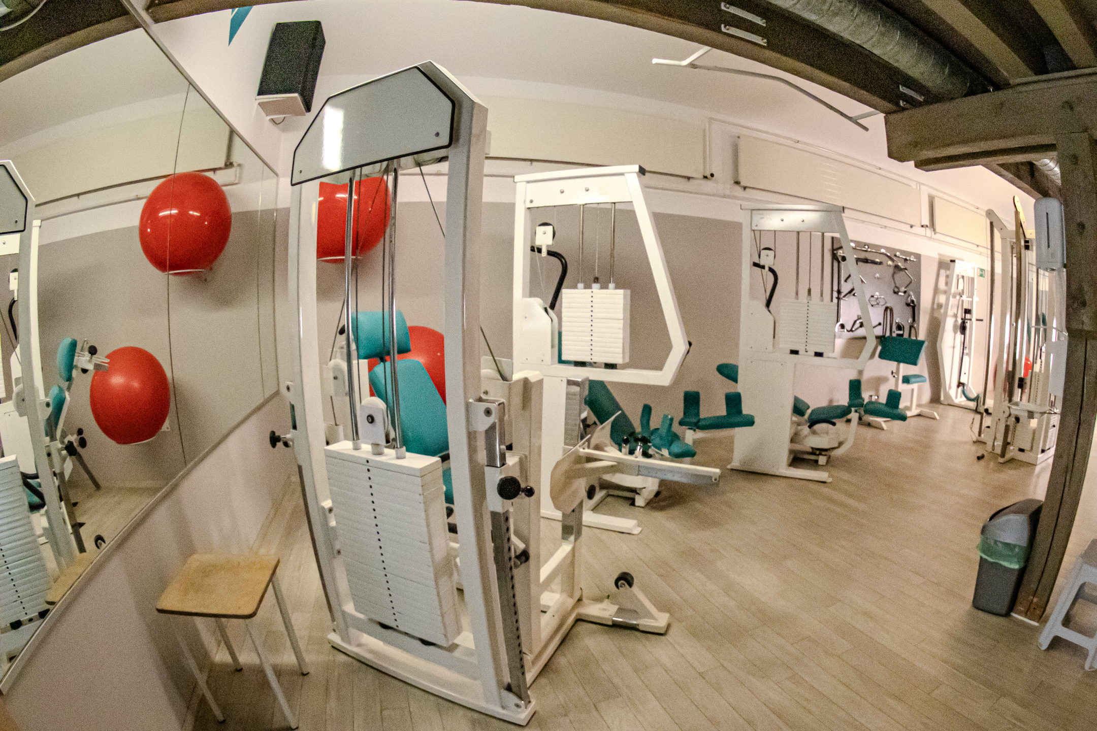 Ein gesammter Fitnessraum mit Kraftgeräten, Trainingsgeräten, roten Gymnastikbällen und Spiegeln an der Wand.