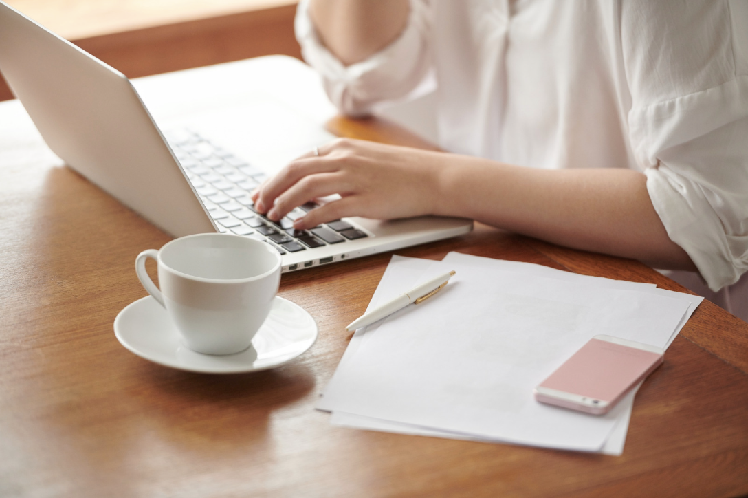 person working on a laptop with notebook, phone and coffee on the desk