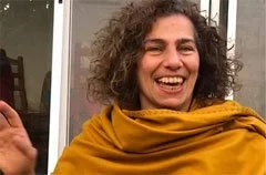 Mujer sonriendo con cabello rizado, con sudadera amarilla.