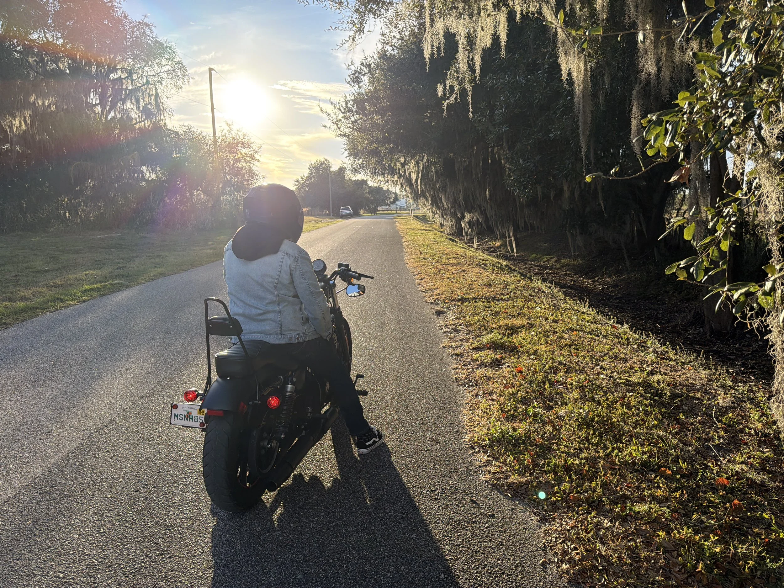 Person riding a motorcycle down a quiet country road in warm morning light