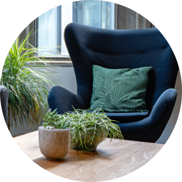 A cozy blue armchair with a green pillow in a room with a large window and potted plants