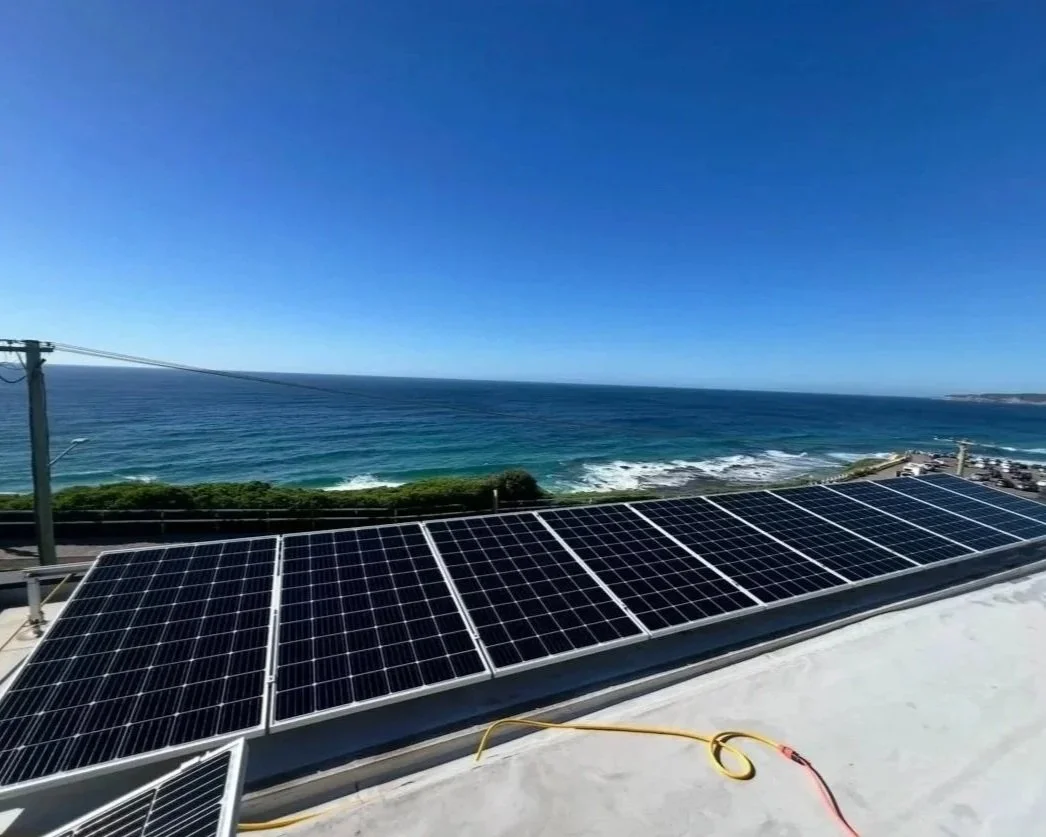 Solar panels installed on a rooftop overlooking the ocean with a clear blue sky.