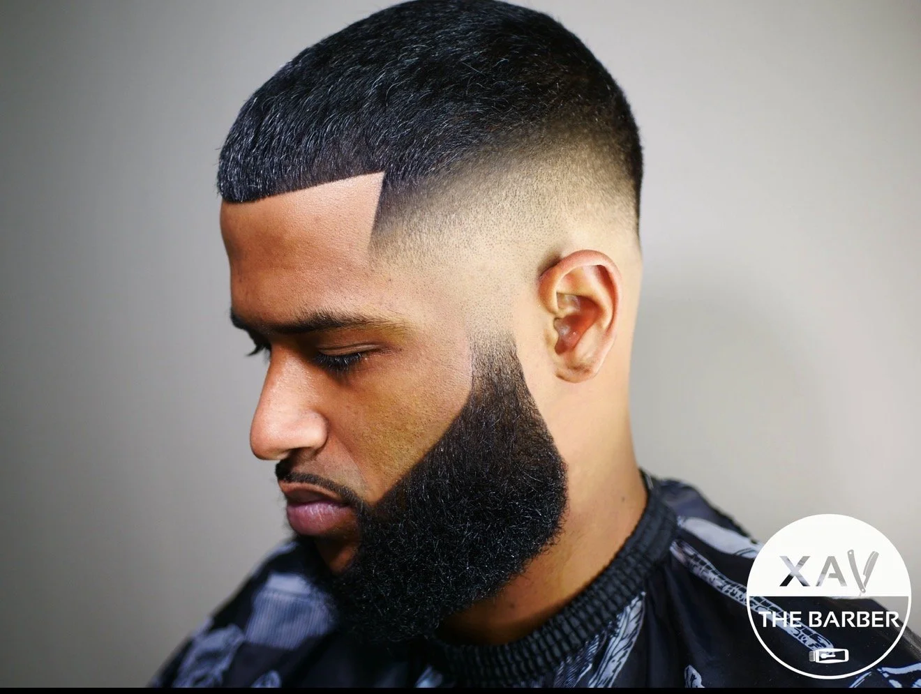 Close-up of a man's profile showcasing a detailed, artistic haircut and beard style at a barbershop.