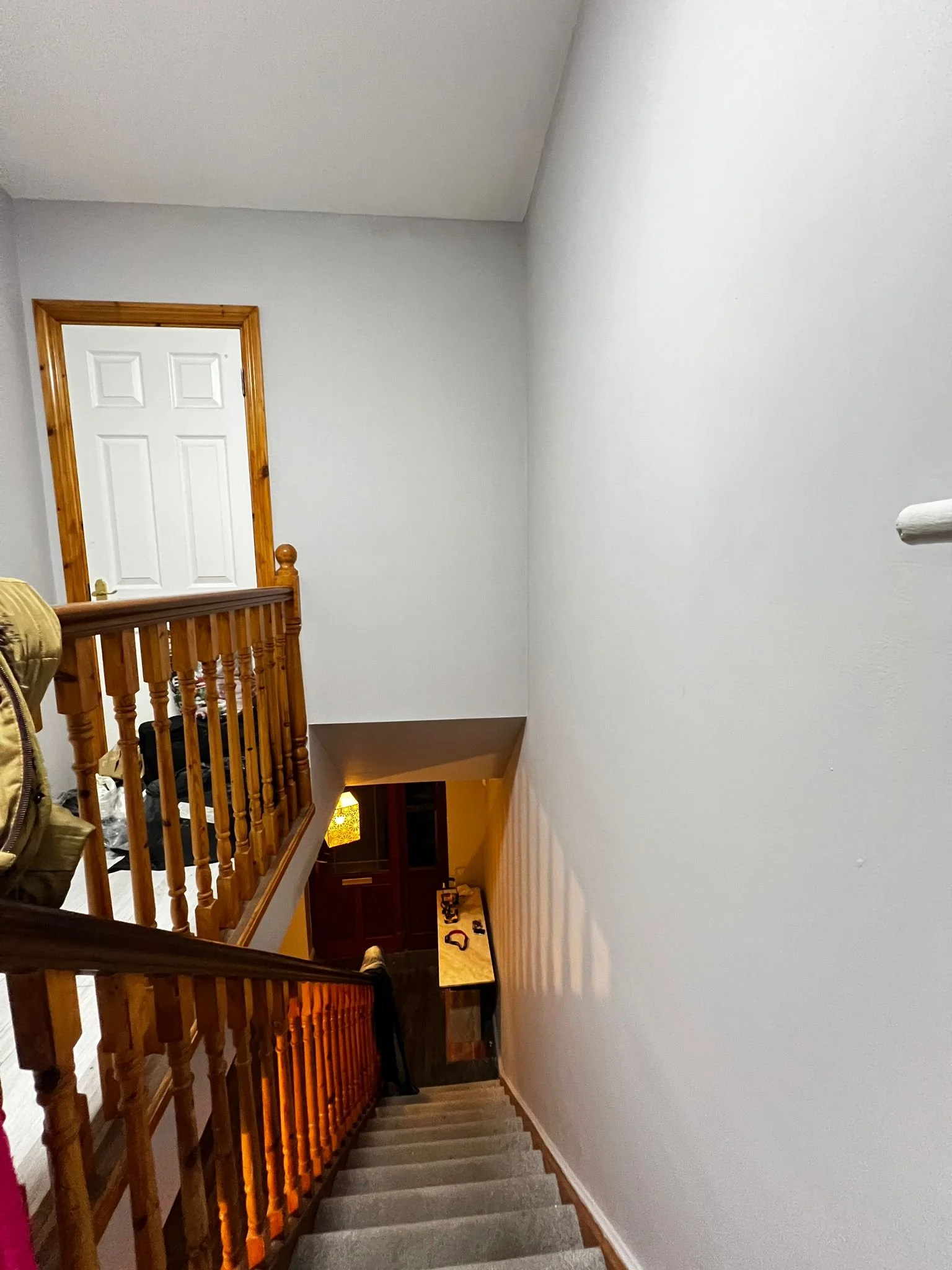 View of a staircase with wooden railings leading down to a door with a small hanging lamp in the background.