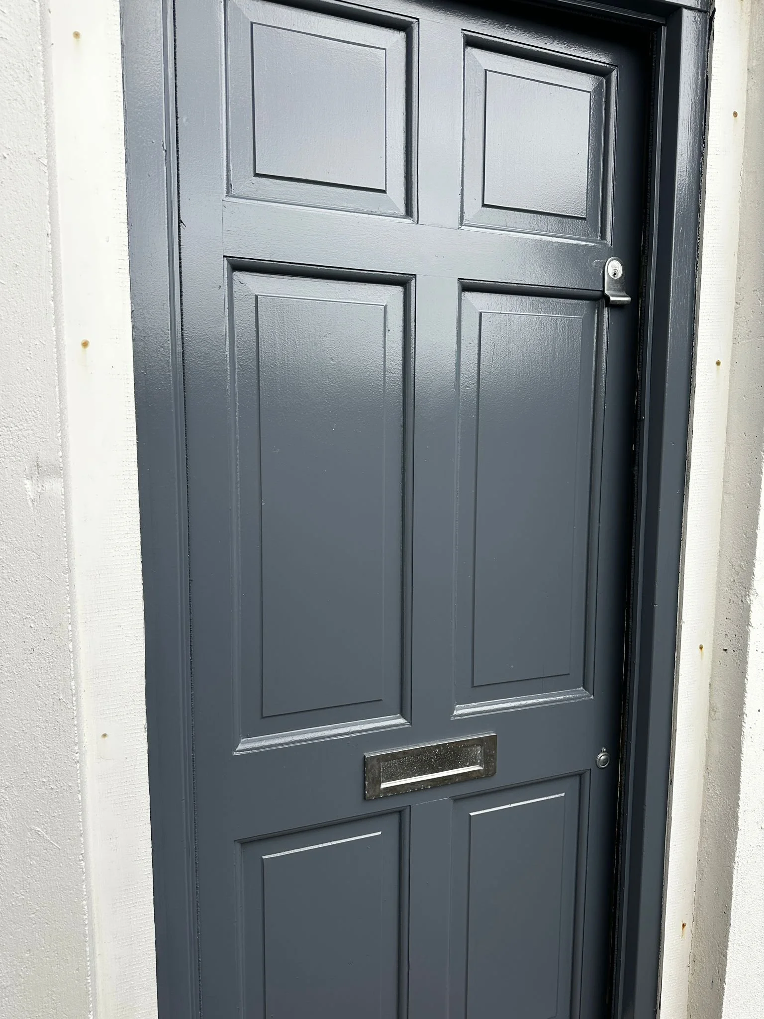 A black front door with six raised rectangular panels, a silver lock, and a mail slot, surrounded by a white frame.