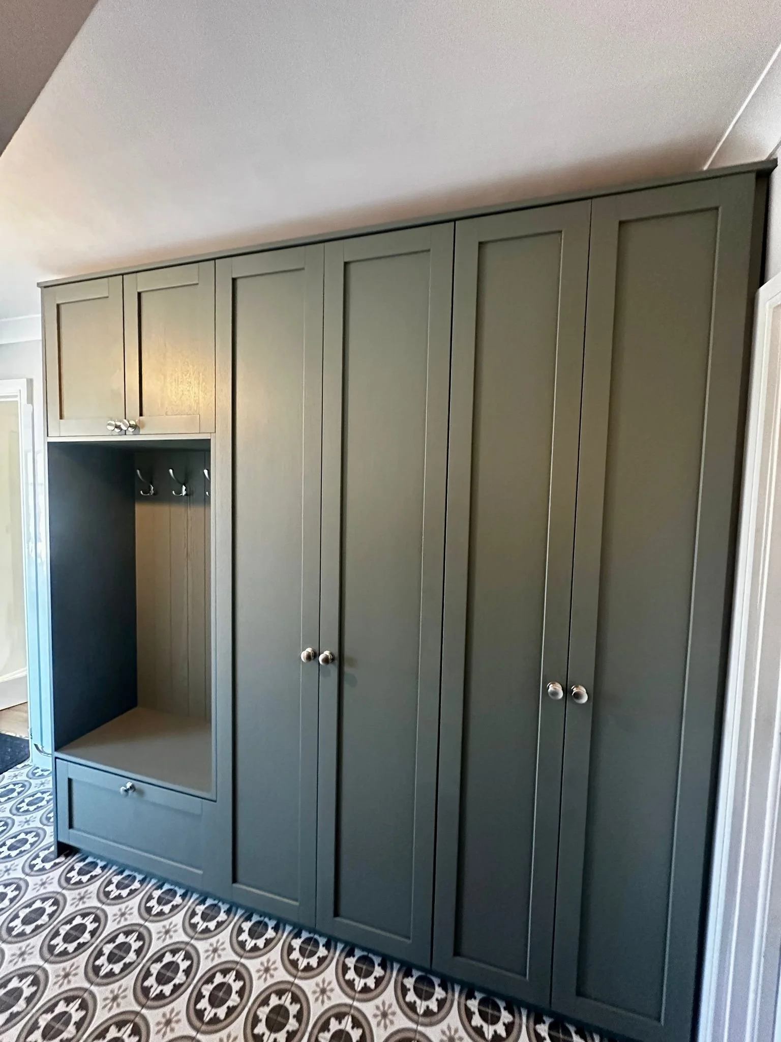 Green built-in wardrobe with multiple doors and a drawer at the bottom, located in a room with patterned black and white tile floor.