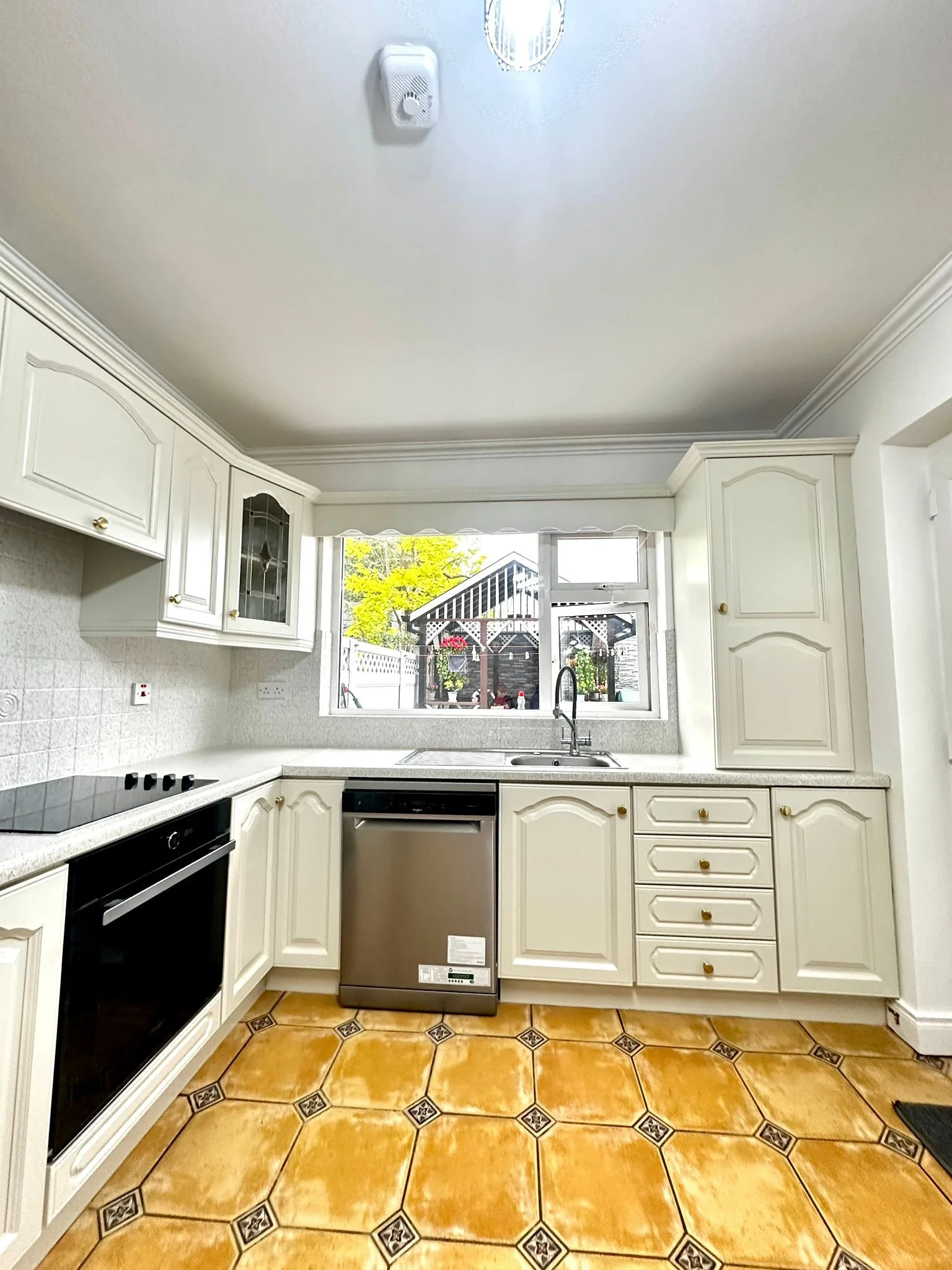 Kitchen with white cabinets, black and stainless steel appliances, a window overlooking a backyard with a shed and outdoor plants, and brown patterned tile flooring.
