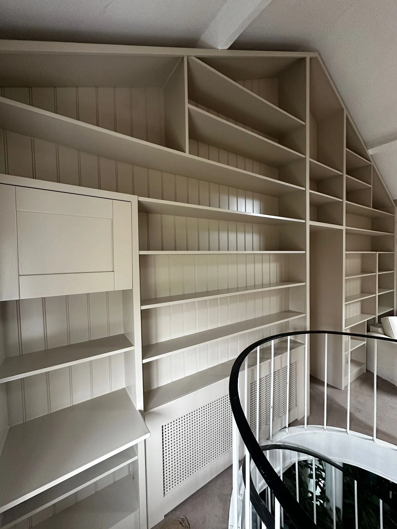 Empty white built-in wall shelves and radiator cover near staircase inside a home.