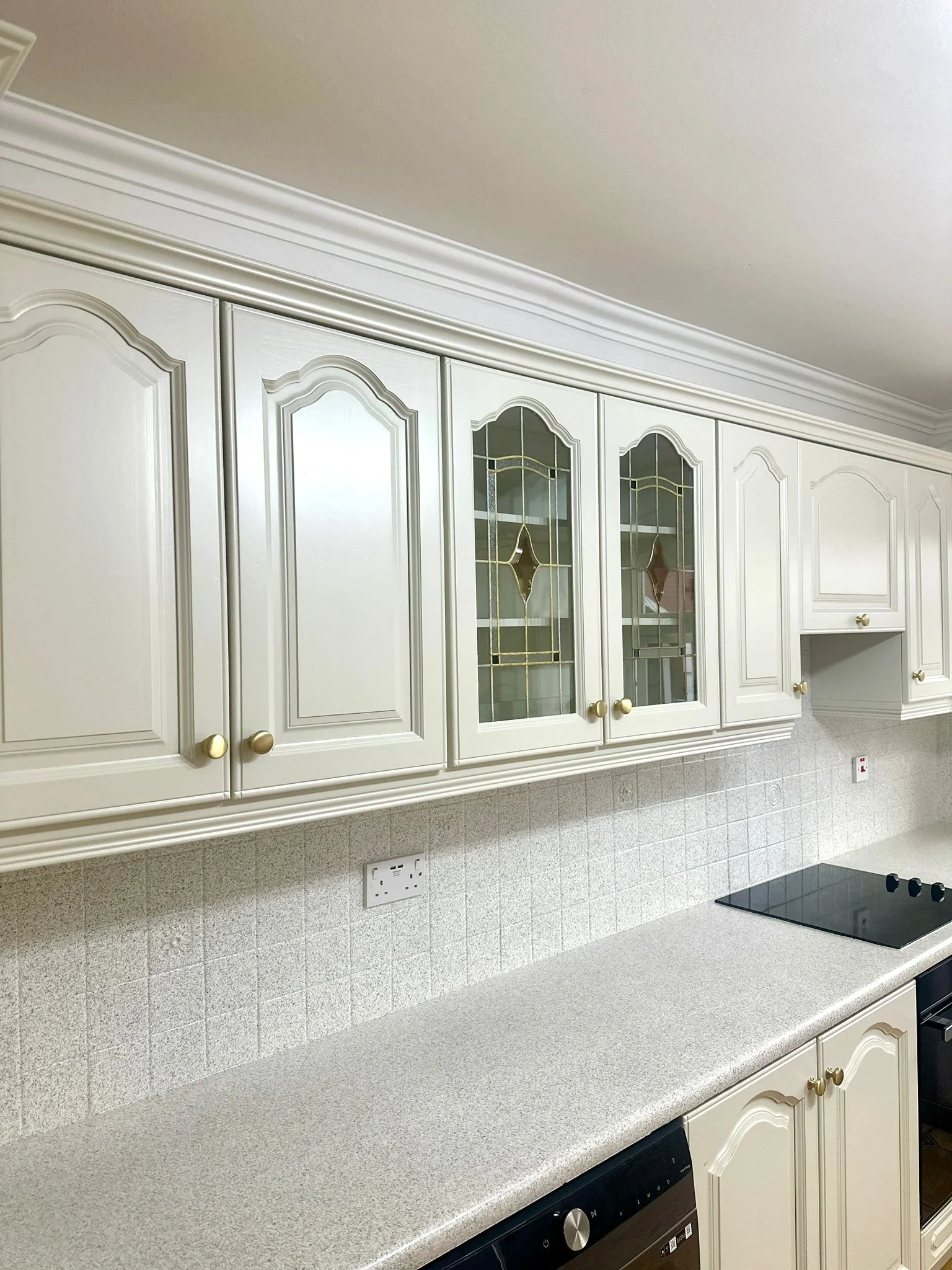 Cream-colored kitchen cabinets with gold knobs, a white countertop, and a gray tile backsplash behind an electric cooktop.