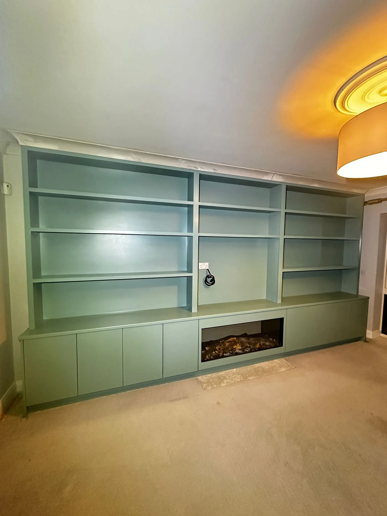 Empty built-in green bookshelf with closed cabinets at the bottom, situated along a beige wall in a living room.