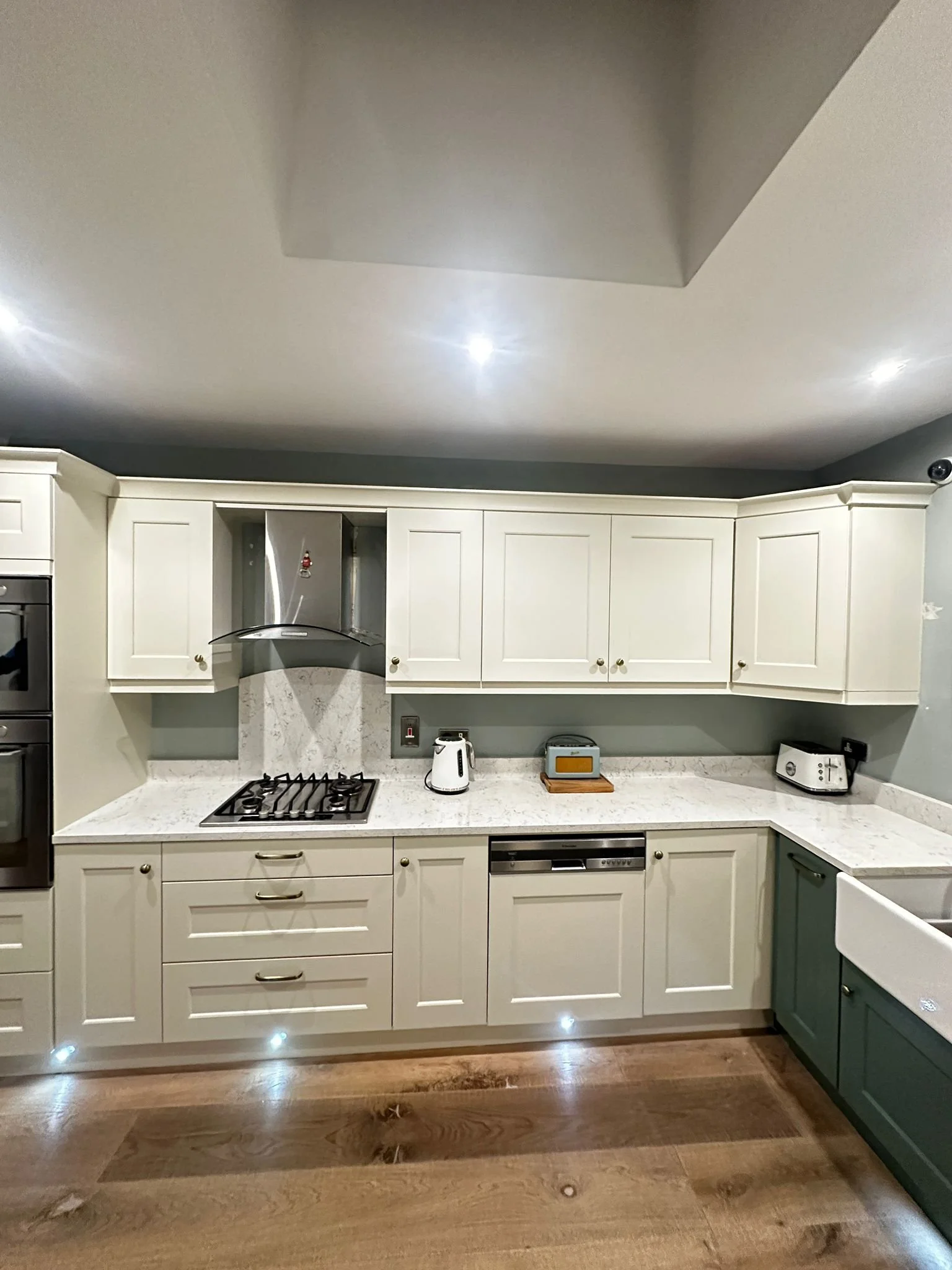 Modern kitchen with white cabinets, a gas stove, a tea kettle, a toaster, and wooden flooring.