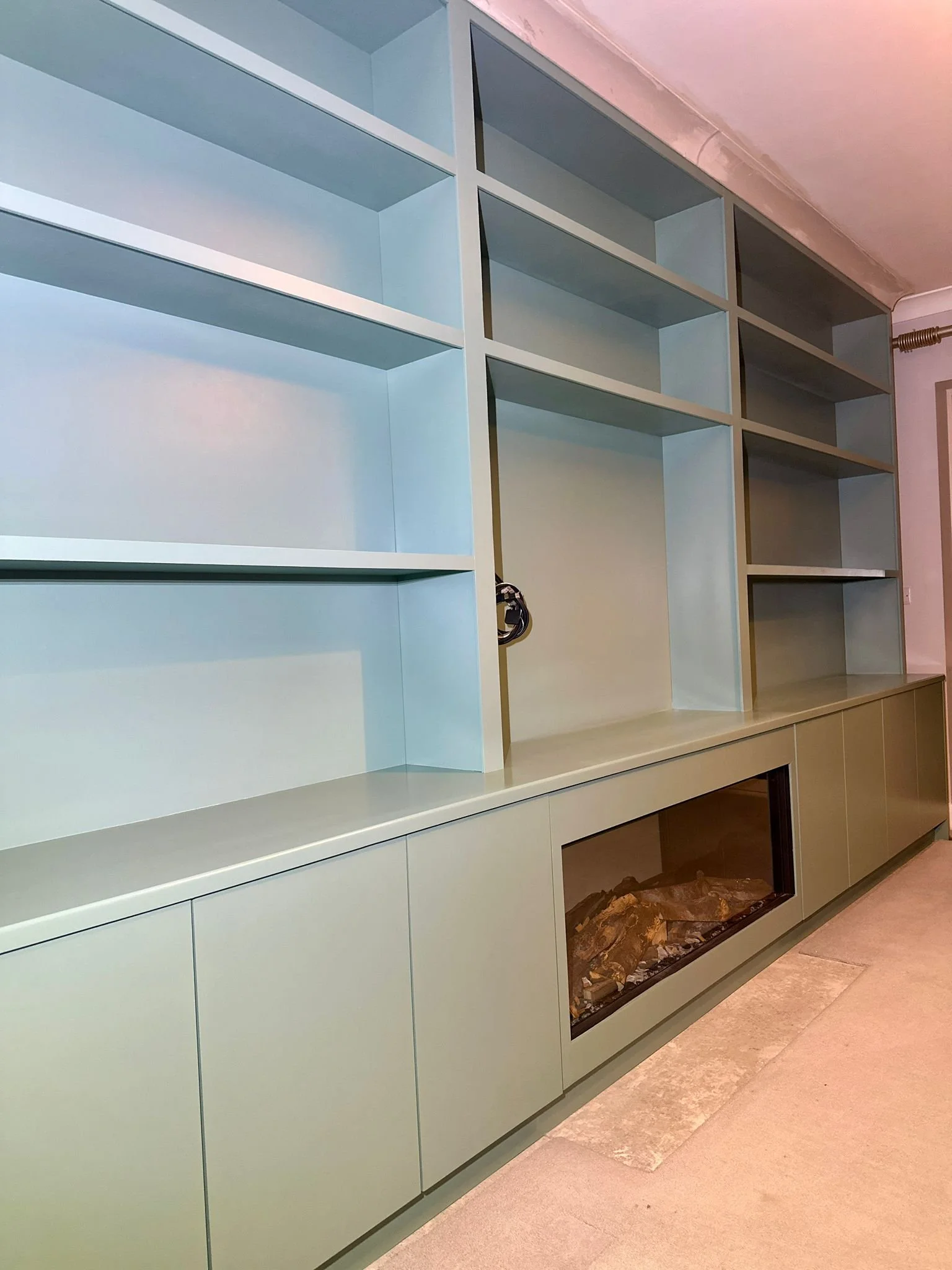 Empty light green bookshelf with a built-in fireplace at the base.