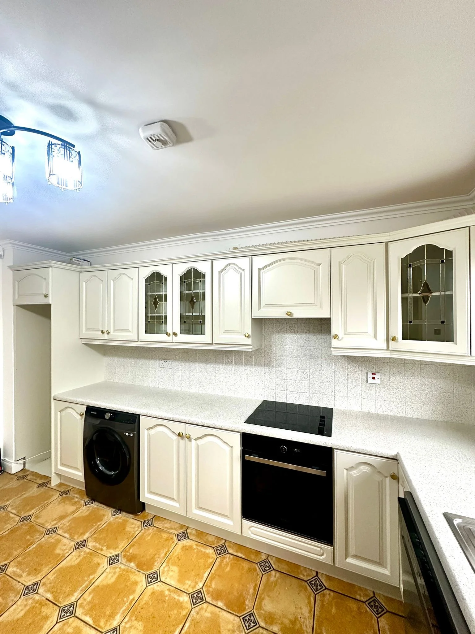 Kitchen with white cabinets, beige countertops, electric stovetop, black oven, washing machine, and tiled floor.