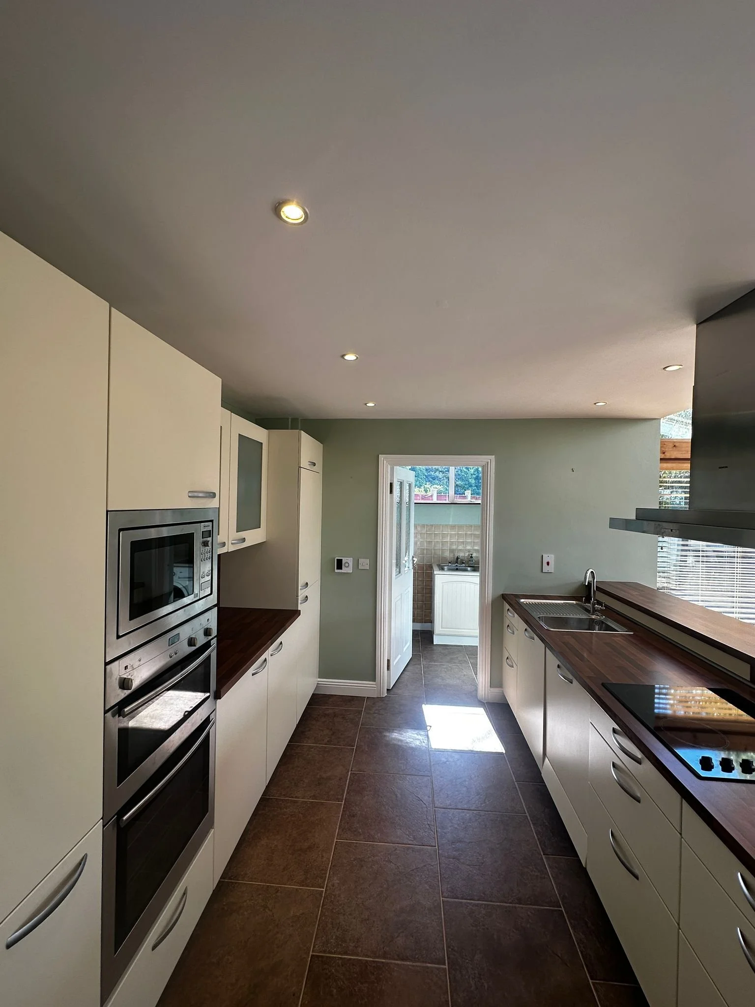 Modern kitchen with dark wood countertops, white cabinets, tile flooring, and a view into a small sunny laundry area.