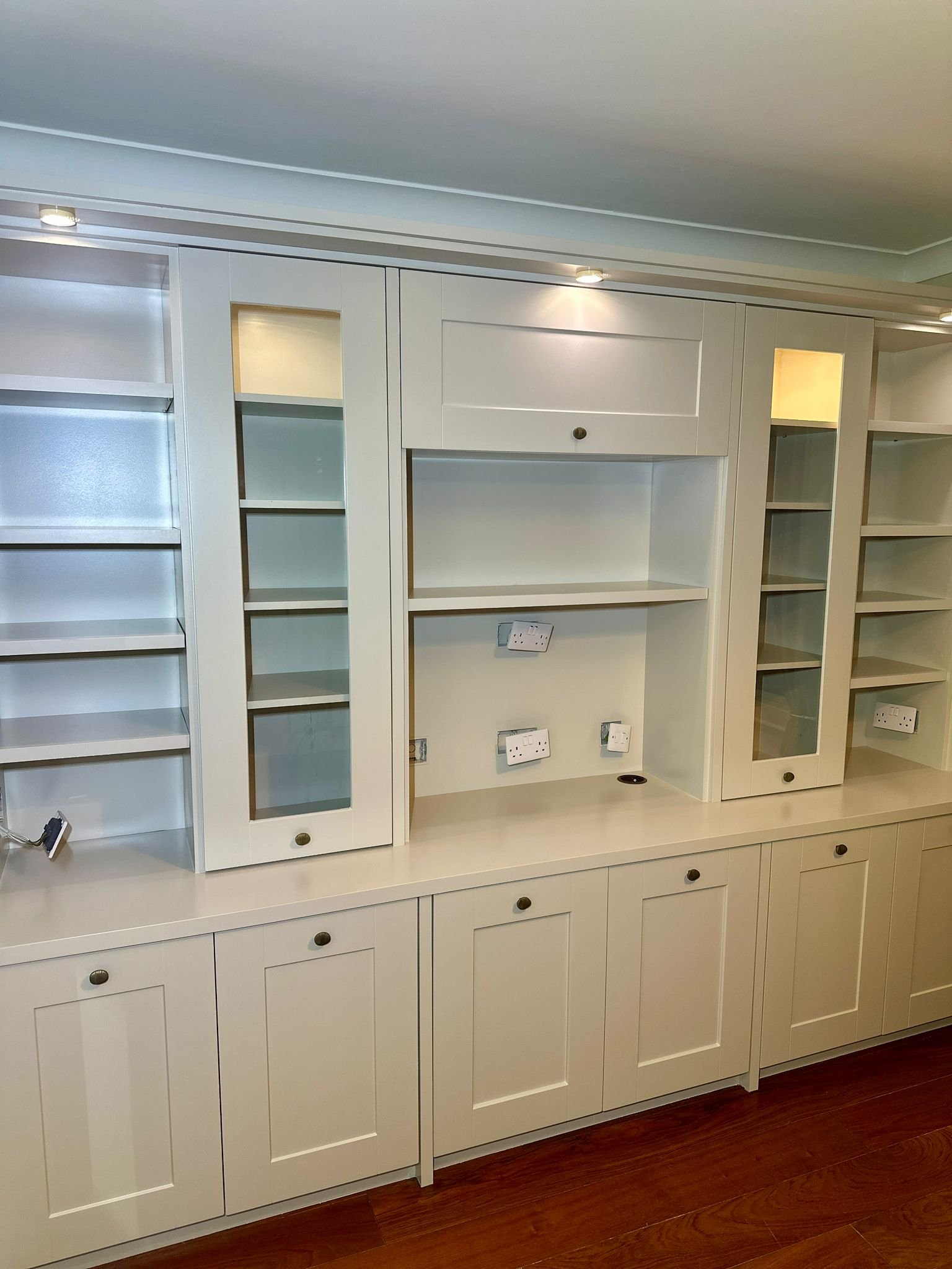 Empty built-in white cabinets and shelves with electrical outlets and a wooden floor.