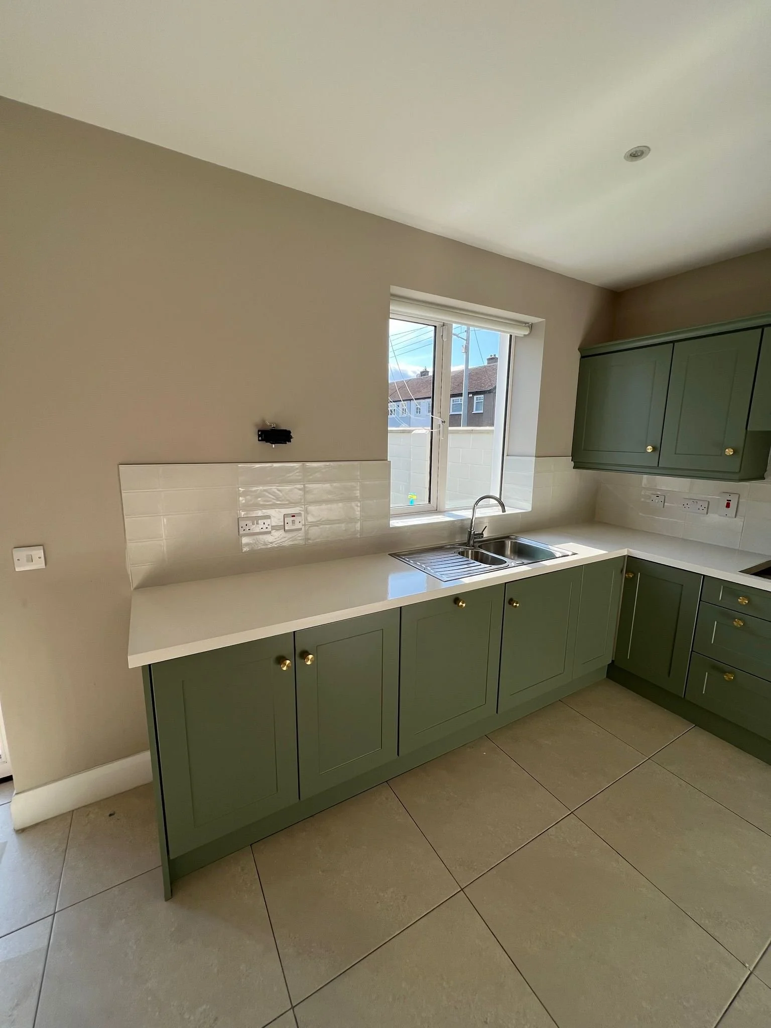 Modern kitchen with green cabinets, white countertop, stainless steel sink, window, and tiled backsplash.