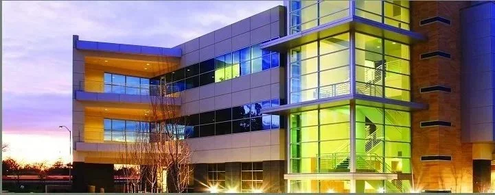 Modern multi-story office building with glass windows and a glass elevator shaft, illuminated during sunset.