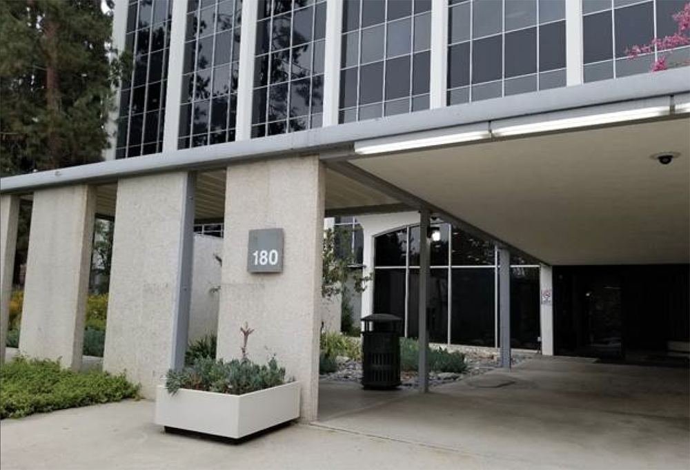 Building with large glass windows, a gray sign showing the number 180, and a covered parking area underneath.