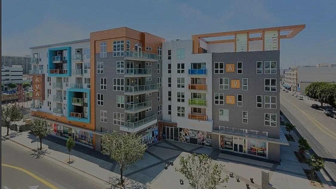 New multi-story residential building with commercial spaces on the ground floor, trees, and a street with cars in an urban area.