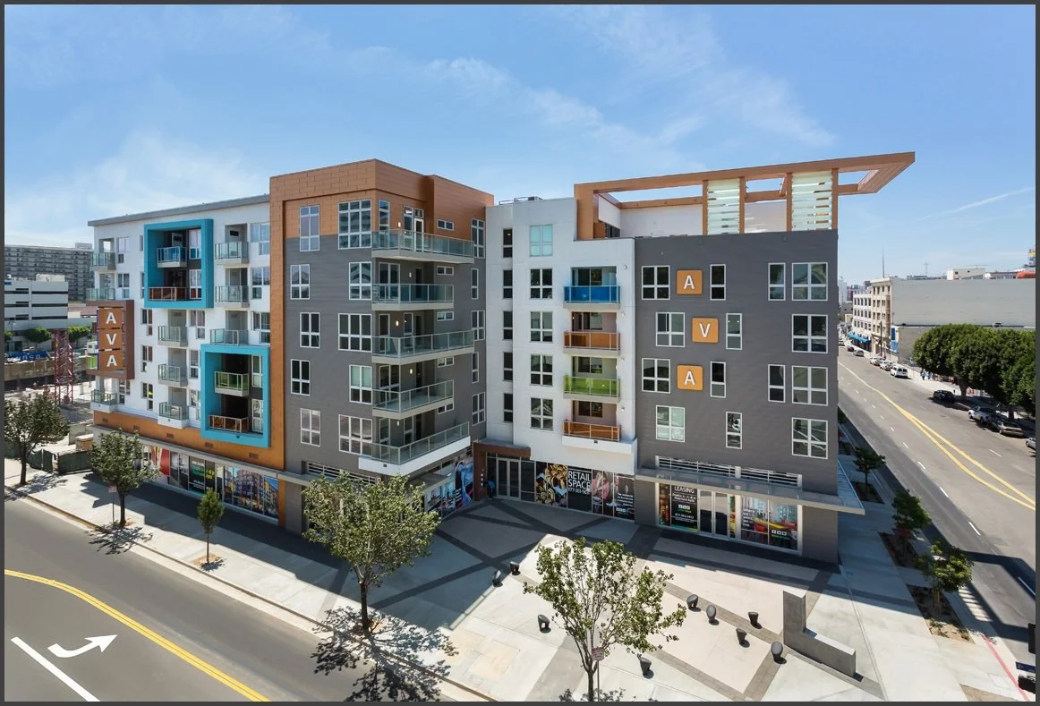 Modern multi-story apartment building with retail space on the ground floor, surrounded by trees and streets, under a blue sky.