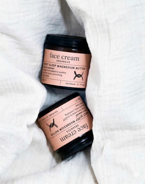 Two black jars of face cream with pink labels, placed on white fabric.