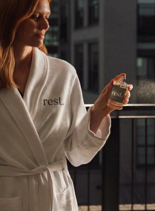 A woman in a white robe labeled "rest" is holding a bottle of perfume or spray.