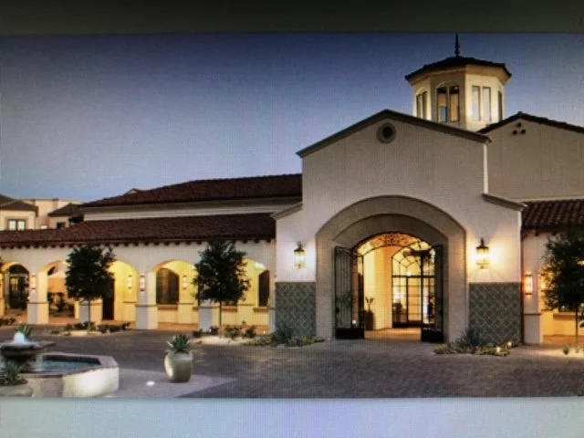 Exterior view of a Mediterranean-style building with white stucco walls, arched windows and doorways, and a tower with a dome on top, at dusk.