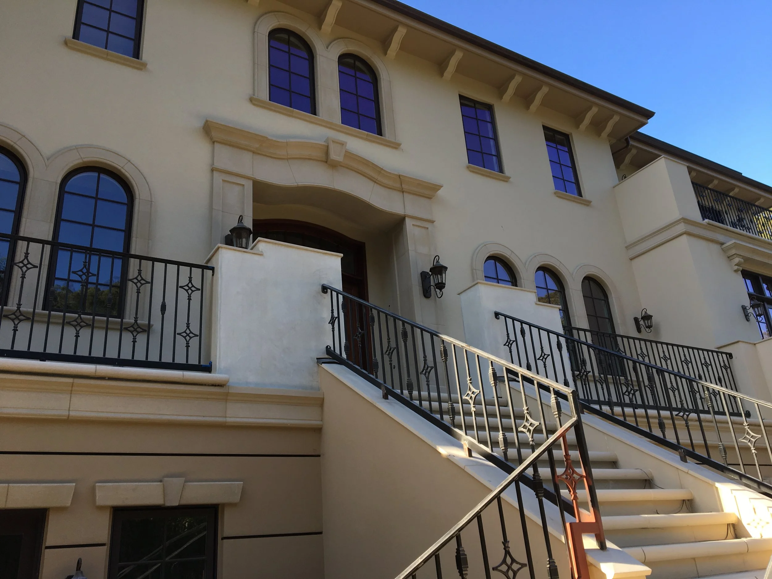 Exterior view of a light-colored multi-story house with arched windows, a staircase, and decorative black metal railings.