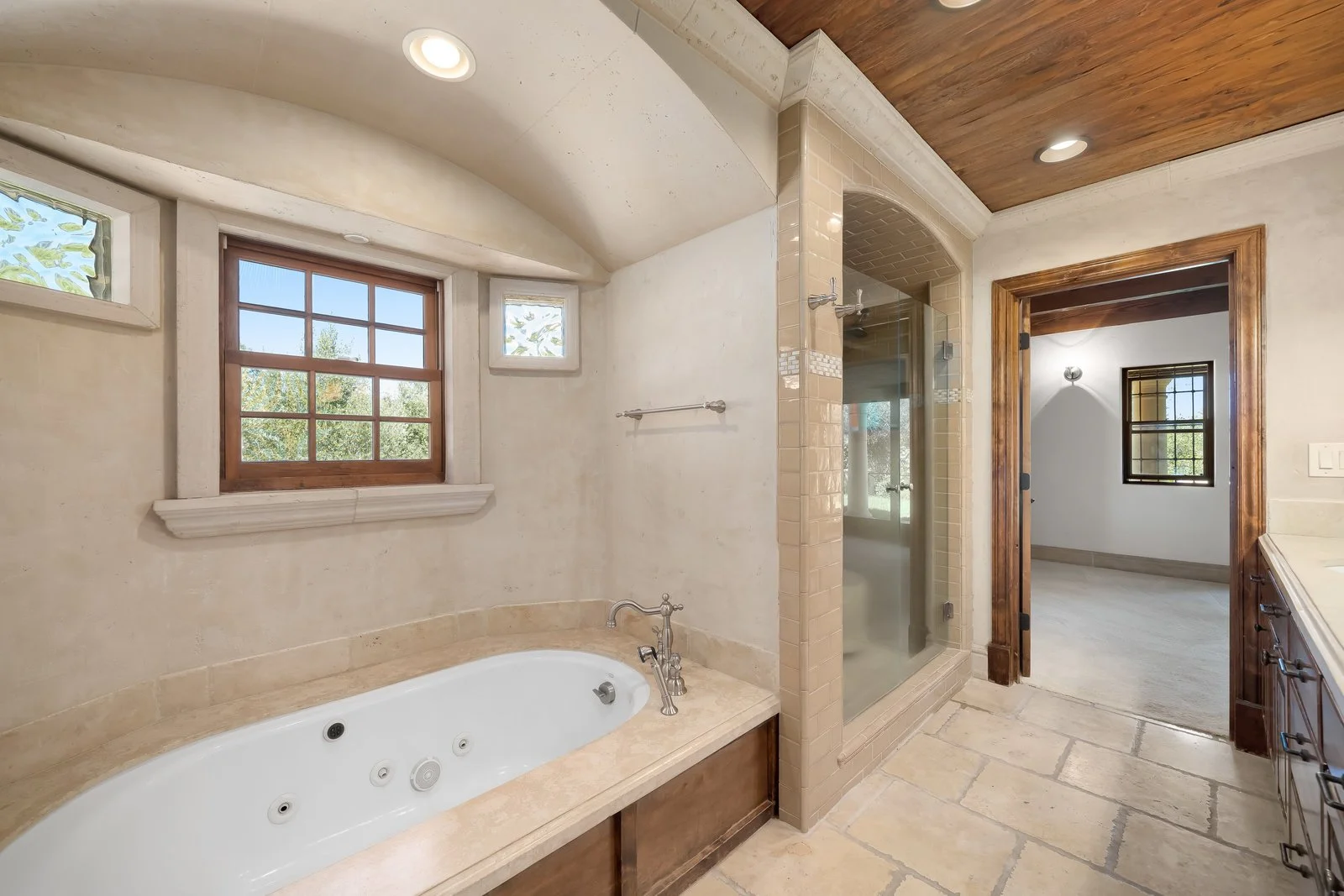 Bathroom with a bathtub, walk-in shower, and small windows with trees outside