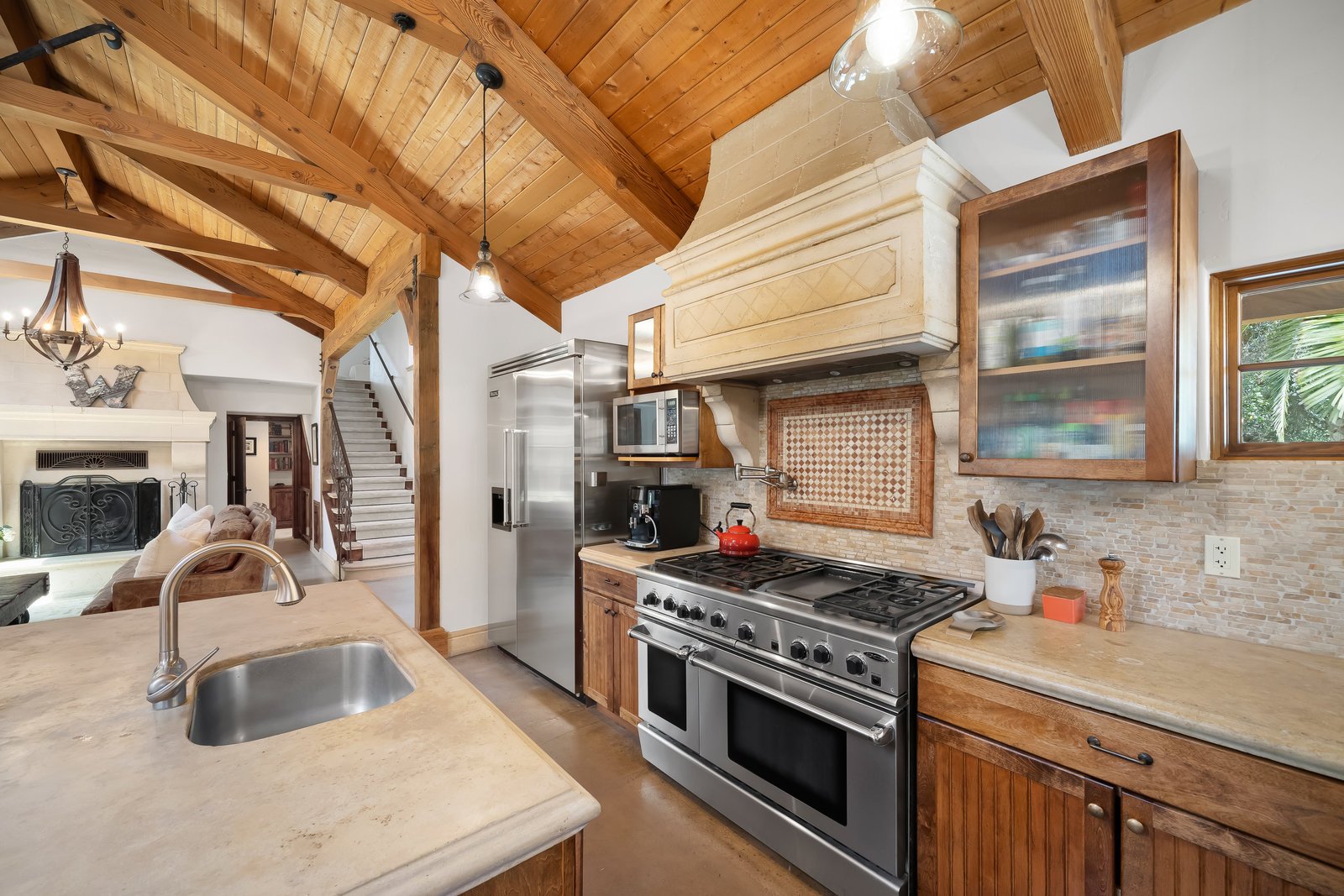 Kitchen with wooden ceiling beams, stainless steel fridge, microwave, red kettle, stove, and beige stone countertops