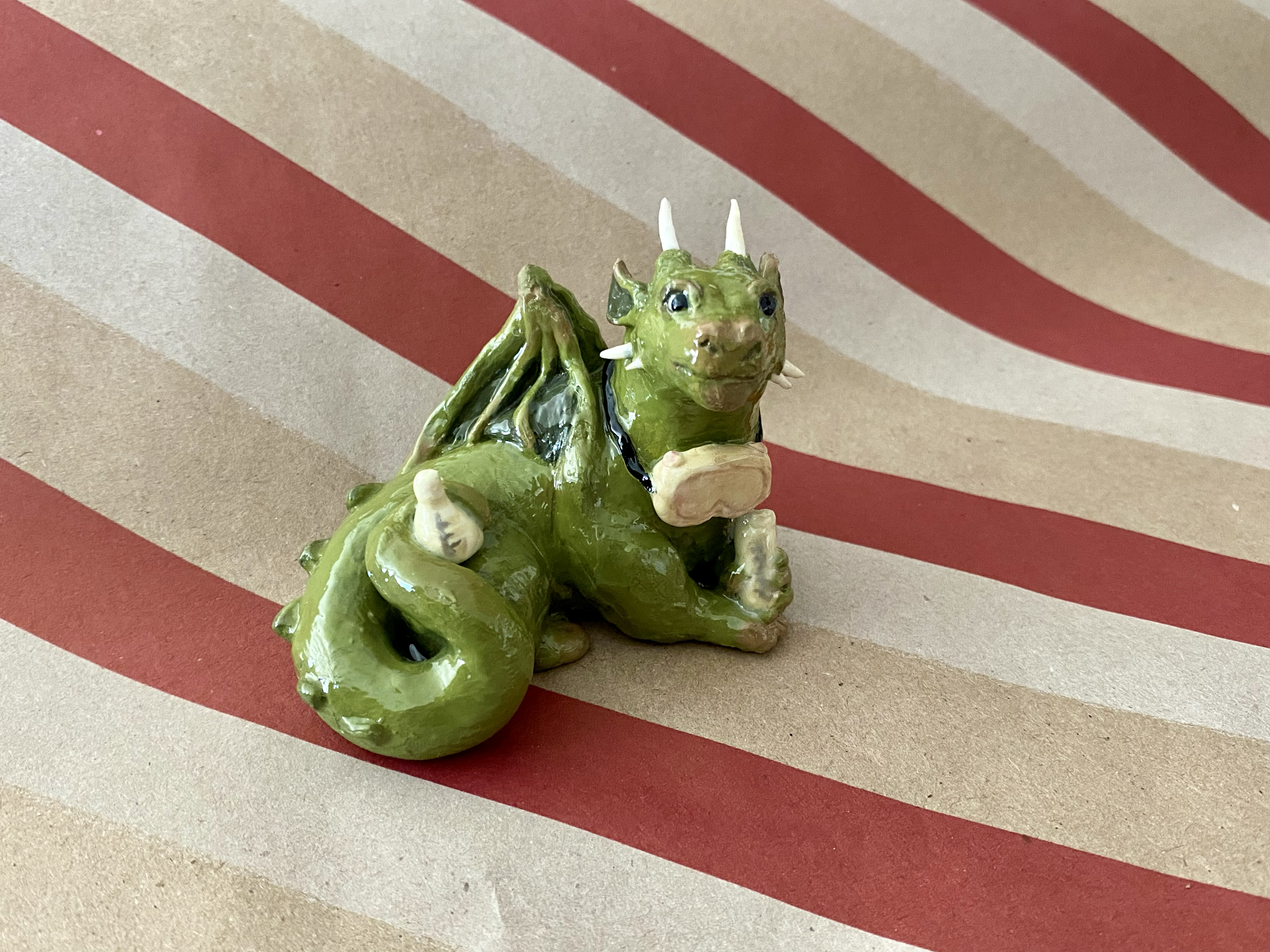 Green polymer clay dragon made to look like a scientist, with a goggles and a set of beakers, against a backdrop of red and brown christmas paper.