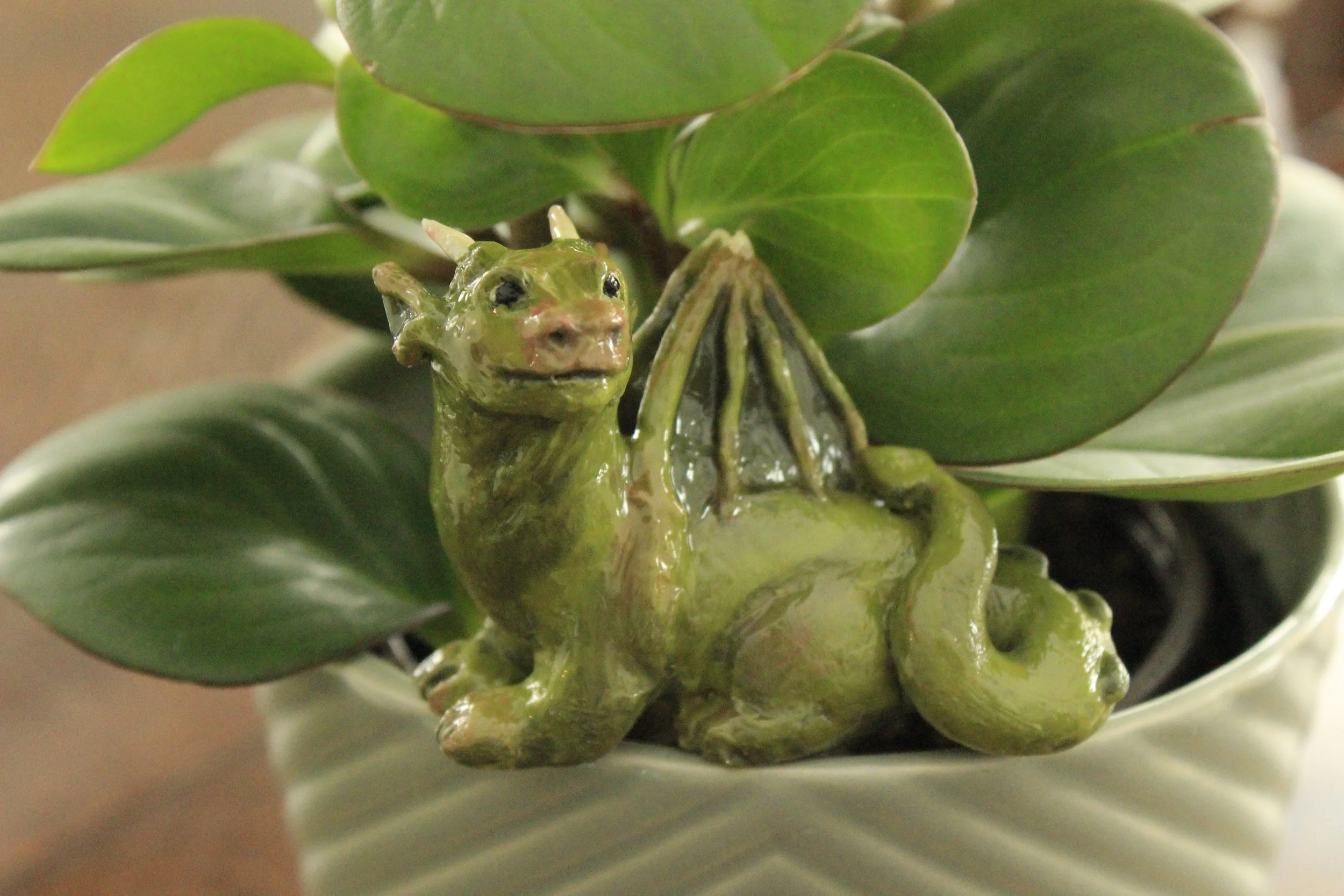 Polymer clay dragon sculpture of a green dragon sitting on the edge of a potted houseplant.
