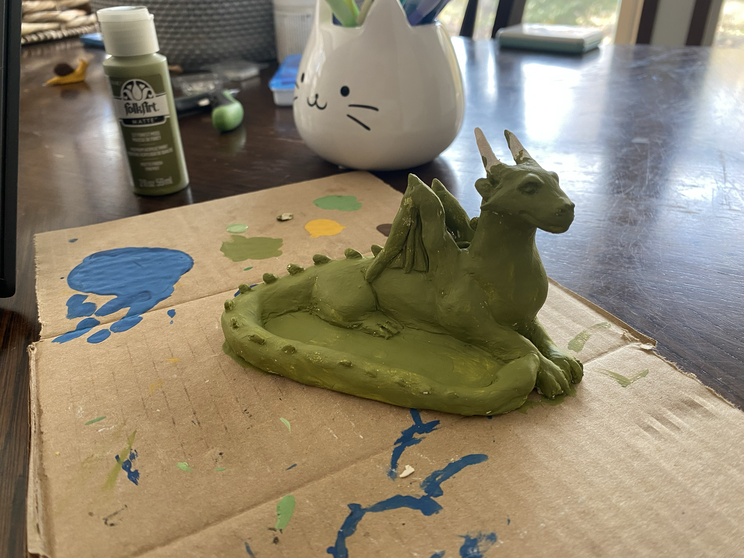Half finished dragon sculpture being painted green on a work surface that is covered with splashes of paint.