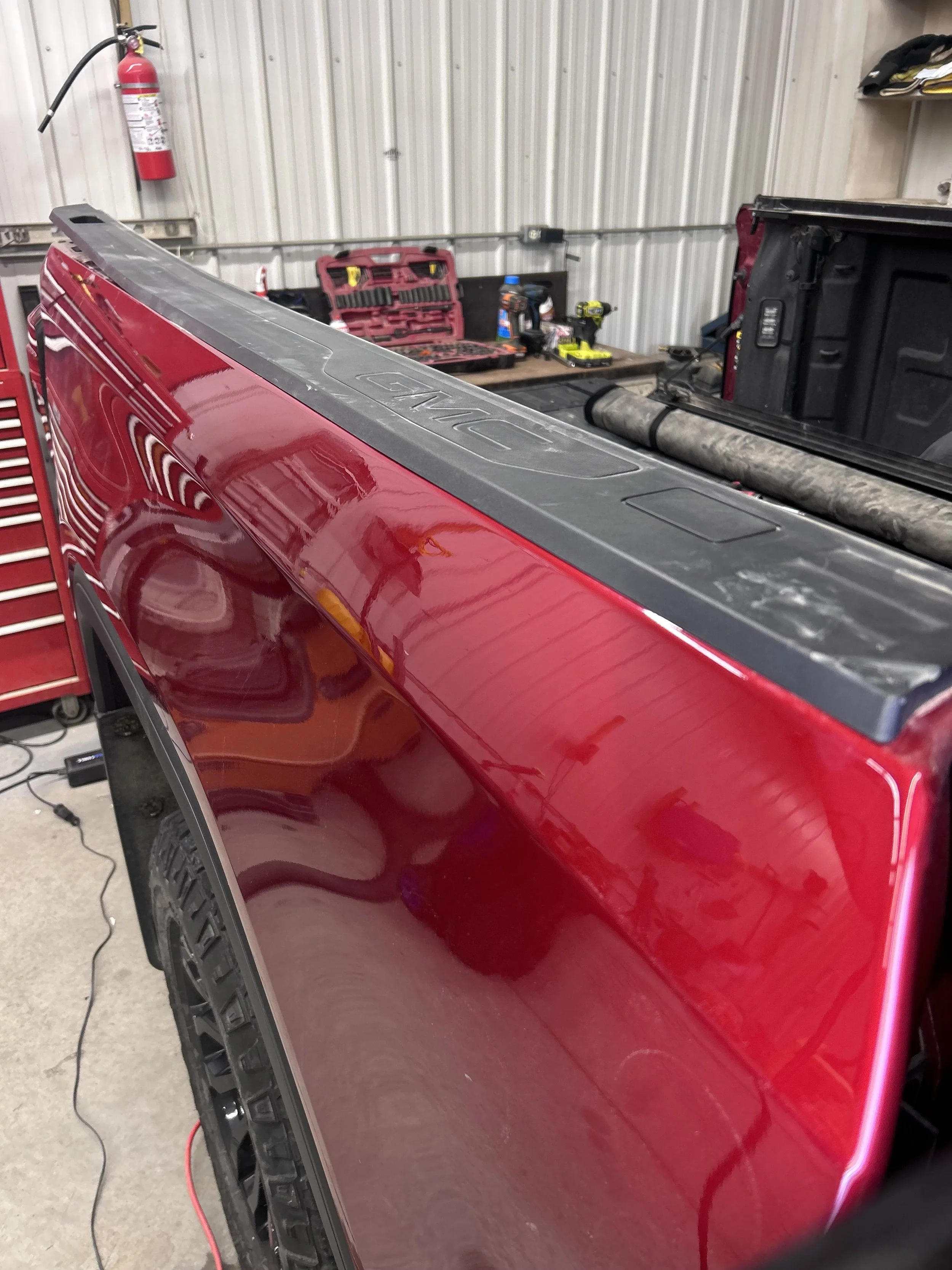 Close-up of the side of a red truck bed with a black toolbox and workshop tools in the background.