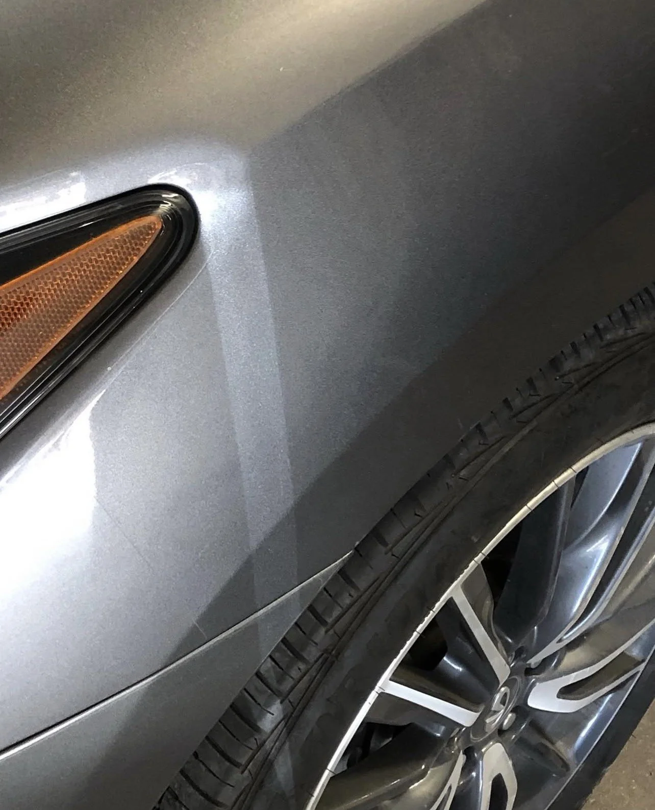 Close-up of a gray car's front tire, wheel, fender, and side marker light.
