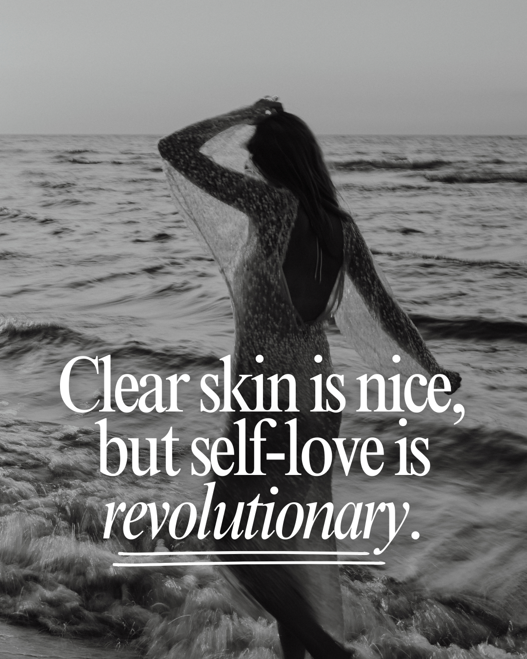 A woman standing in the ocean at sunset or sunrise, holding her hair with one hand, with a text overlay that reads, "Clear skin is nice, but self-love is revolutionary."