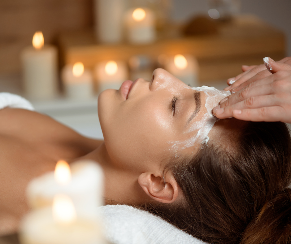 A woman receiving a facial treatment in a spa with lit candles in the background.