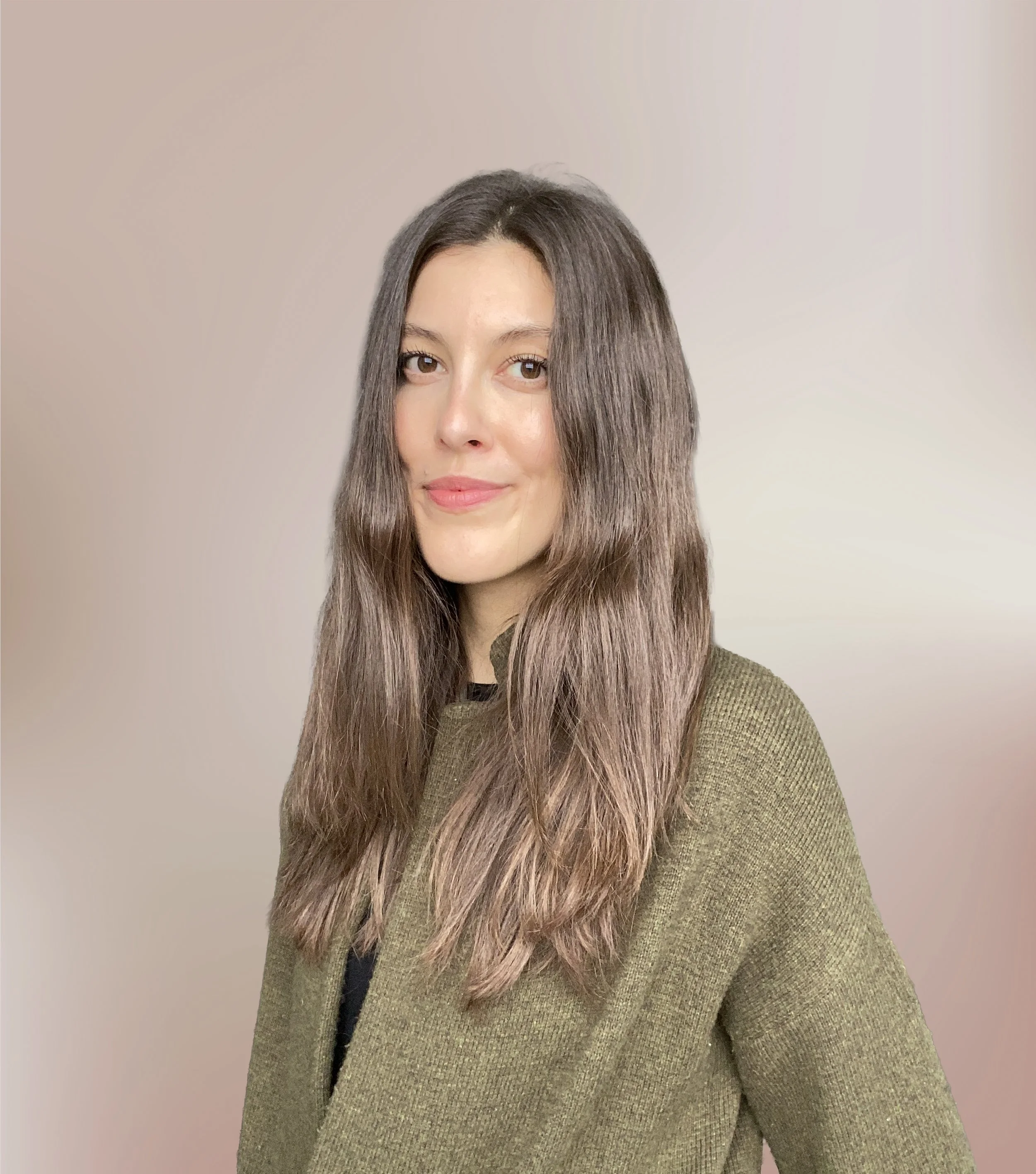 A young woman with long, wavy brown hair and fair skin, wearing an olive green sweater, looking at the camera with a slight smile, standing against a neutral background.