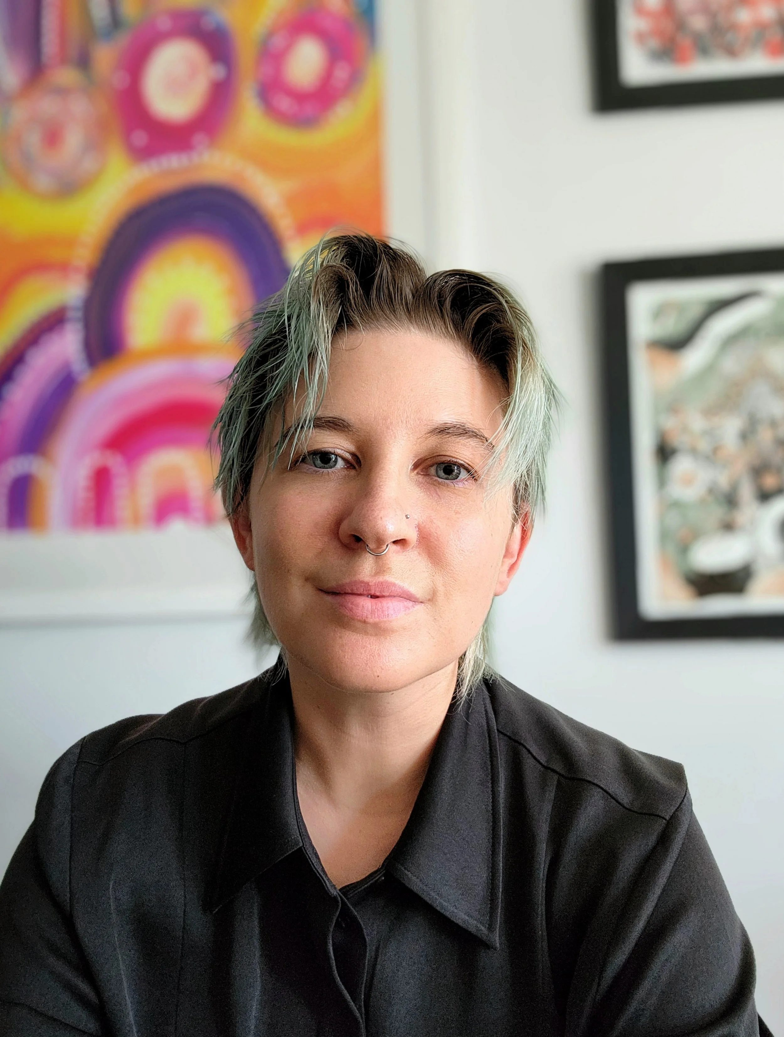 The semi-smiling face of Eli Sutherland sitting in front of brightly coloured art.