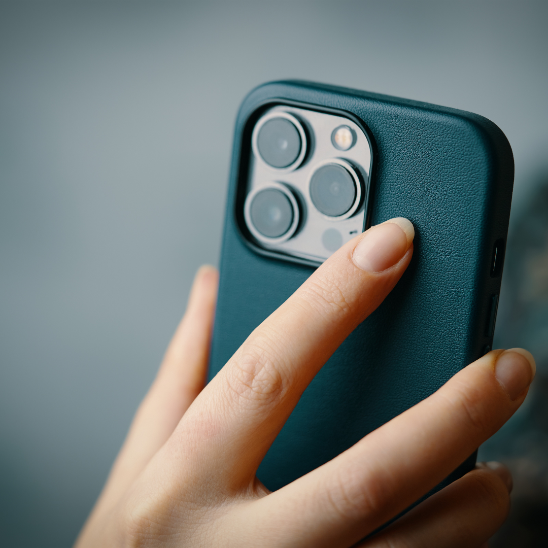 Close-up of a person's hand holding a smartphone with a textured blue case, showing the camera lenses on the back.