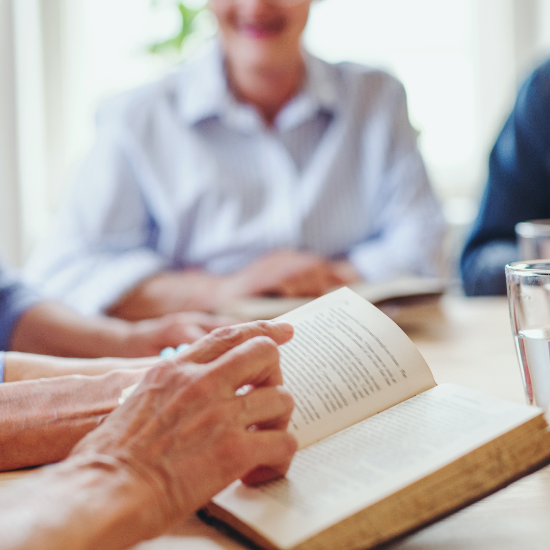 People sitting around a table, discussing or reading a book, with glasses of water on the table.