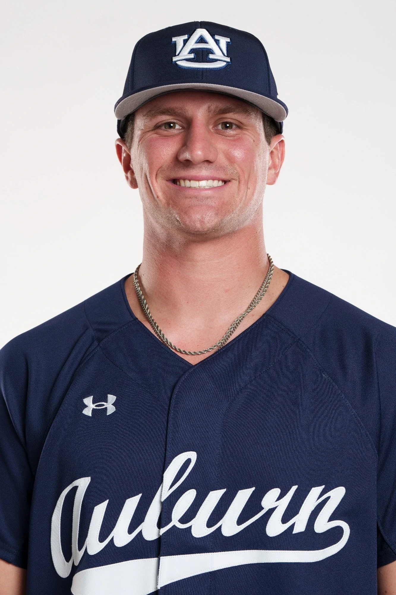 A young man wearing a navy blue sports jersey with white lettering and a matching navy blue cap with the Auburn University logo.