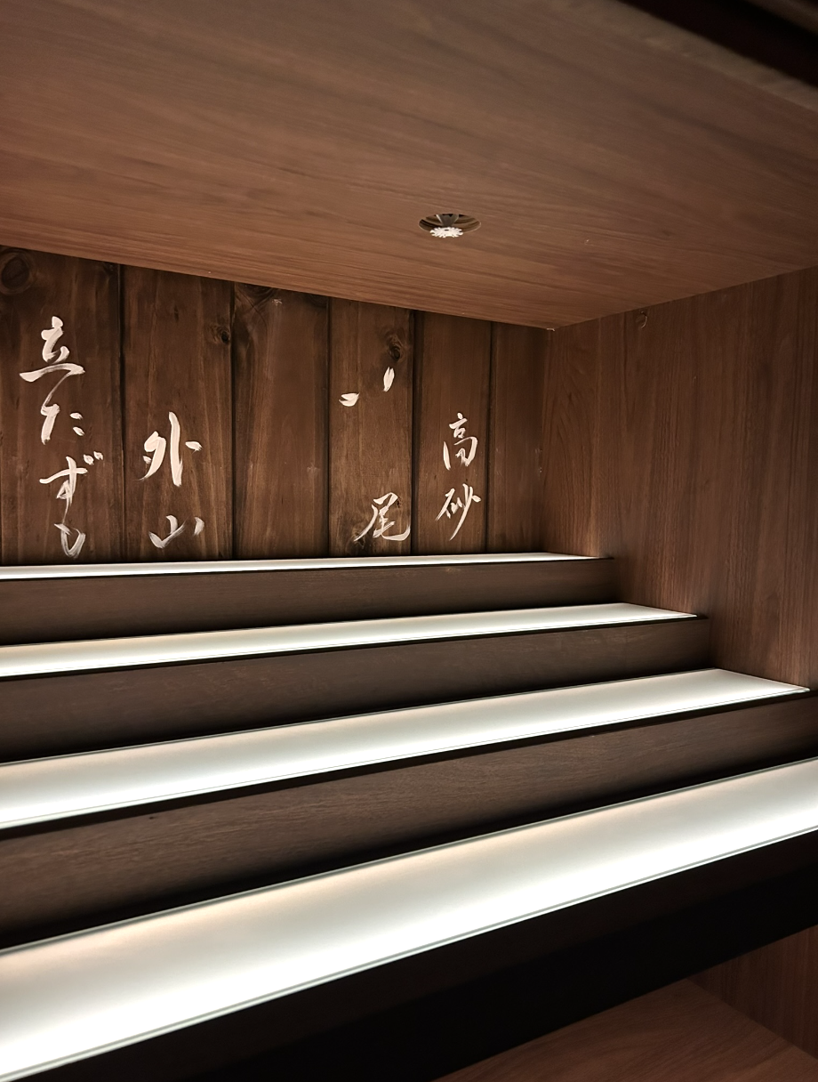 Wooden stairs with built-in lighting and Japanese calligraphy on the wall behind.