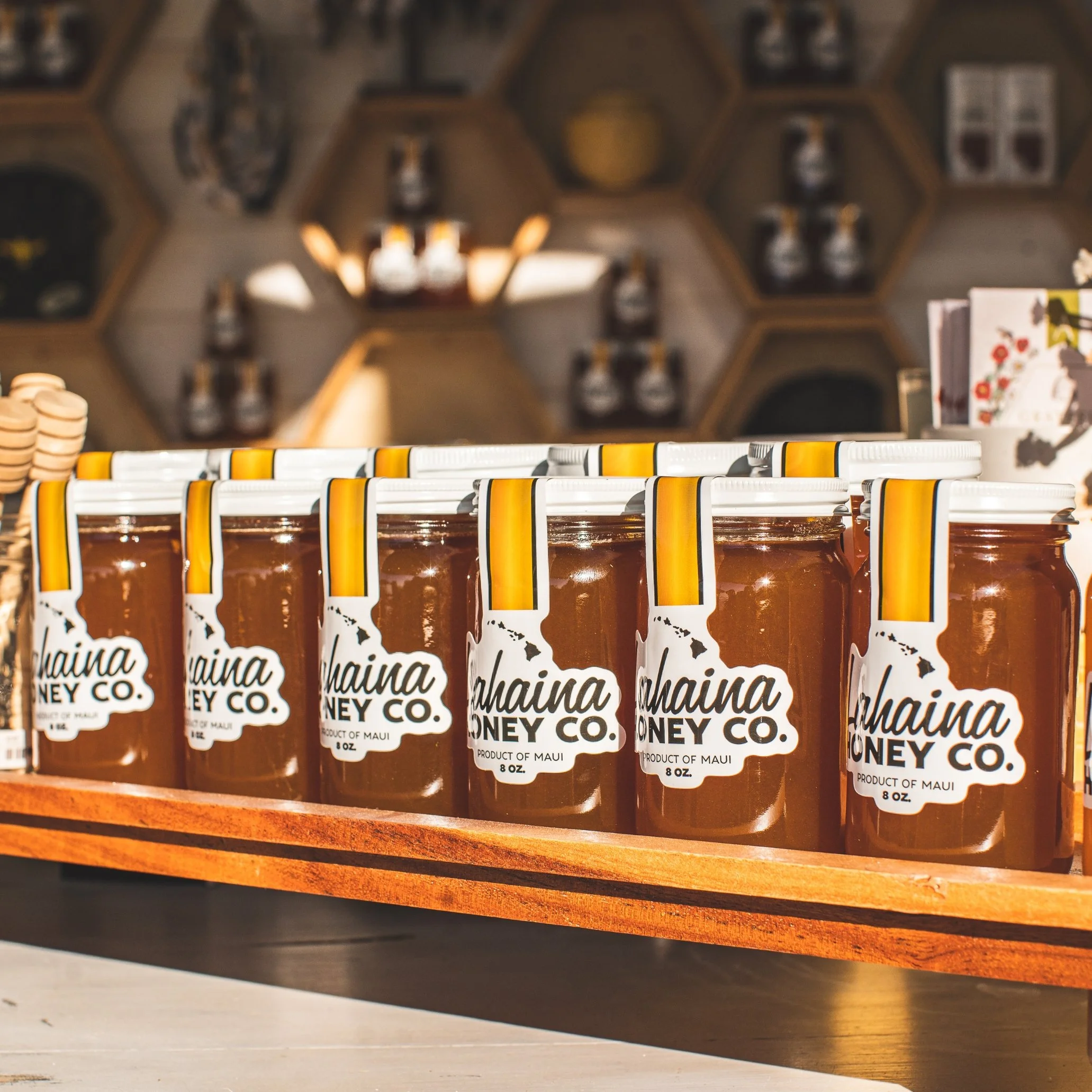 Rows of small jars labeled 'Hawaiian Honey Co.' on a wooden shelf, with blurred background showing a honey-themed display.