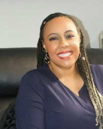 BS Eventful, LLC co-founder, woman with braided hair and earrings, smiling, wearing a navy top, sitting on a black leather couch.